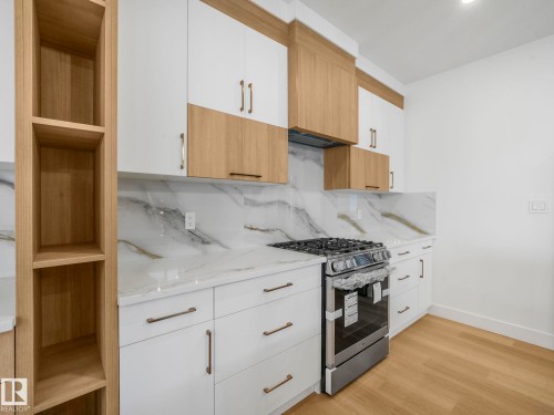 Contemporary kitchen featuring a gas range, white cabinetry with bronze hardware, light wood-finish flooring, and white countertops with matching backsplash - 6125 Crawford Drive, Edmonton, AB - Indoor Photo Showing Kitchen