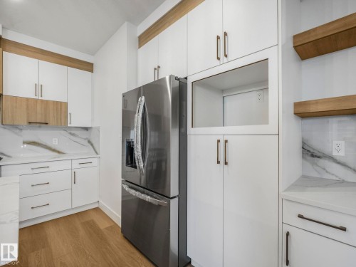 Modern kitchen featuring a stainless steel refrigerator, white cabinetry with bronze hardware, and wood-finish accents - 6125 Crawford Drive, Edmonton, AB - Indoor Photo Showing Kitchen