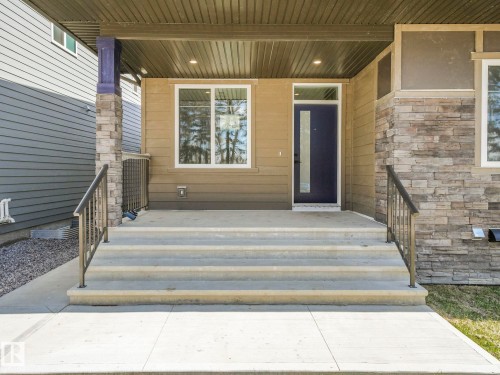 Front entrance featuring a covered porch, stone accent pillars, and a dark entry door with a vertical glass insert - 6125 Crawford Drive, Edmonton, AB - Outdoor With Exterior