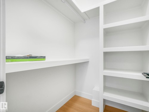 Walk-in closet featuring built-in shelving, a hanging rod, light wood-finish flooring, and white baseboards - 6125 Crawford Drive, Edmonton, AB - Indoor With Storage