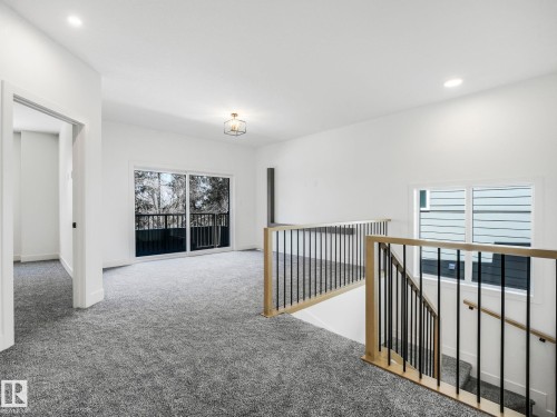 Open concept secondary living area featuring plush gray carpeting, a sliding glass door leading to an exterior balcony, and a contemporary metal and wood staircase railing - 6125 Crawford Drive, Edmonton, AB - Indoor Photo Showing Other Room