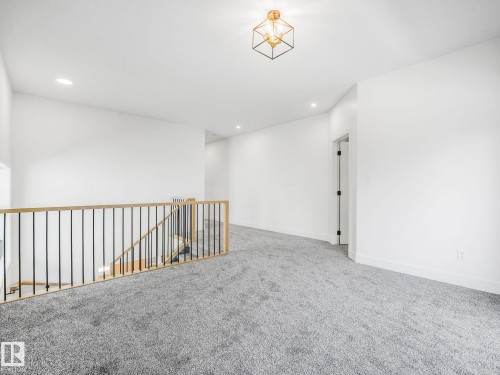 Carpeted landing featuring a wooden handrail with black iron balusters, recessed lighting, and a contemporary gold-tone geometric ceiling fixture - 6125 Crawford Drive, Edmonton, AB - Indoor Photo Showing Other Room