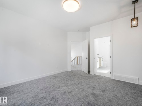 Expansive carpeted room featuring a ceiling-mounted light fixture, white baseboards, and a doorway opening to a bathroom with a vanity and toilet - 6125 Crawford Drive, Edmonton, AB - Indoor Photo Showing Other Room