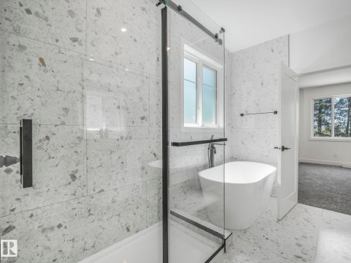 Spacious bathroom featuring a frameless glass shower enclosure with a dark hardware accent, a freestanding soaking tub, and large format terrazzo-style tile flooring and shower surround - 6125 Crawford Drive, Edmonton, AB - Indoor Photo Showing Bathroom