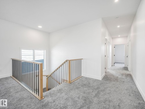 Upper-level landing featuring light gray carpeting, modern staircase with wood and black metal railings, recessed ceiling lighting, and a window with horizontal blinds - 6125 Crawford Drive, Edmonton, AB - Indoor Photo Showing Other Room