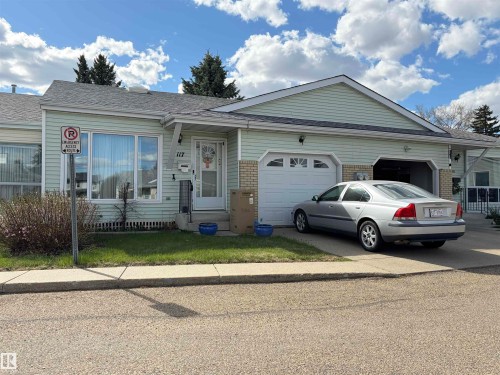 Light green siding exterior with a single-car garage featuring a decorative paneled door - 117 17703 64 Avenue, Edmonton, AB - Outdoor