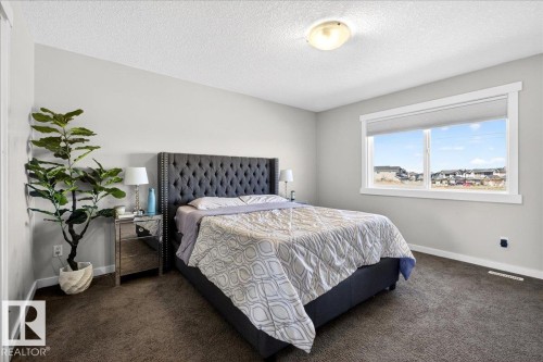 Spacious room featuring neutral painted walls, dark textured carpet, and a large window with white trim - 3936 Claxton Loop, Edmonton, AB - Indoor Photo Showing Bedroom