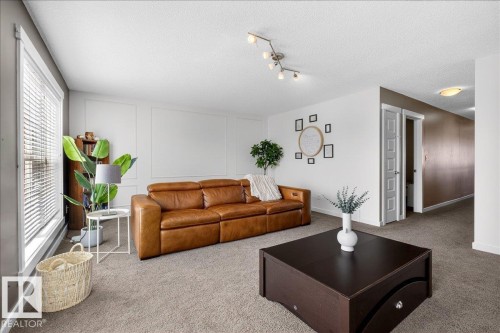 Spacious living area featuring neutral carpeting, a large window with blinds, and white panel accent wall details - 3936 Claxton Loop, Edmonton, AB - Indoor Photo Showing Living Room