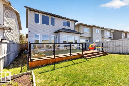 Expansive backyard featuring a manicured lawn, a raised wooden deck with glass panel railing, and a stone retaining wall - 3936 Claxton Loop, Edmonton, AB - Outdoor With Deck Patio Veranda With Exterior