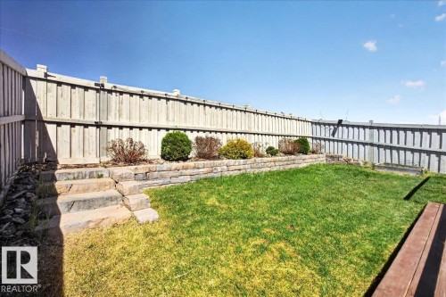 Fenced backyard featuring a tiered retaining wall, stone steps, landscaped garden beds with shrubs, and a grassy lawn - 3936 Claxton Loop, Edmonton, AB - Outdoor