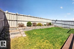 Fenced backyard featuring a tiered retaining wall, stone steps, landscaped garden beds with shrubs, and a grassy lawn - 