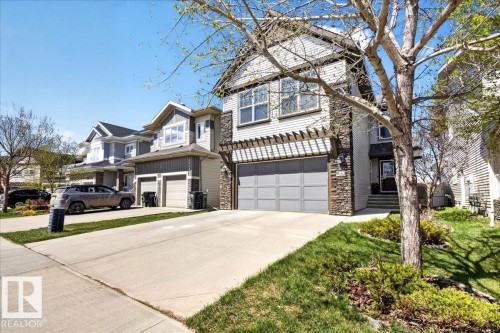 Multi-story residence featuring light-colored siding, a stone facade, and a two-car garage with a pergola accent - 3936 Claxton Loop, Edmonton, AB - Outdoor With Facade