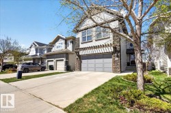 Multi-story residence featuring light-colored siding, a stone facade, and a two-car garage with a pergola accent - 