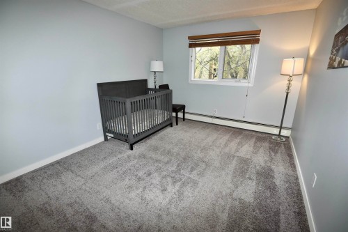Room featuring light gray walls, gray patterned carpeting, and white baseboards - 21 10160 119 Street Nw, Edmonton, AB 