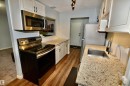 Kitchen featuring wood-finish flooring, light cabinetry with dark hardware, stainless steel appliances, granite-style countertops, and track lighting - 21 10160 119 Street Nw, Edmonton, AB 