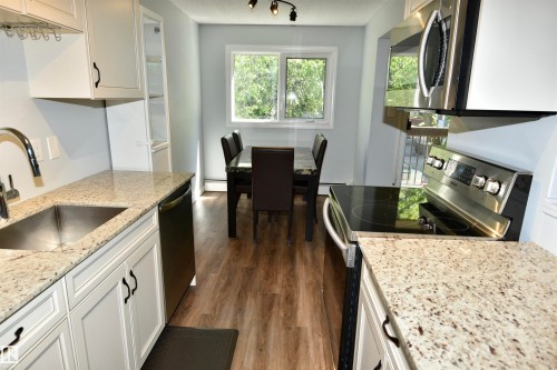 Kitchen featuring granite-style countertops, stainless steel appliances, wood-finish flooring, white cabinetry, and a built-in display cabinet - 21 10160 119 Street Nw, Edmonton, AB 