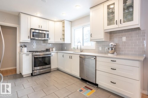 Kitchen featuring white shaker-style cabinetry, stainless steel appliances, light gray subway tile backsplash, light-toned countertops, and rectangular floor tiling - 8239 93A Avenue, Edmonton, AB - Indoor Photo Showing Kitchen With Stainless Steel Kitchen