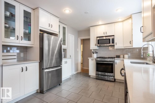 Modern kitchen featuring white shaker cabinetry, stainless steel appliances, light-toned countertops, a subway tile backsplash, and recessed lighting - 8239 93A Avenue, Edmonton, AB - Indoor Photo Showing Kitchen With Stainless Steel Kitchen