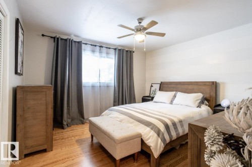 Room featuring wood-finish flooring, a ceiling fan with integrated lighting, and a single window with drapes and sheer curtains - 8239 93A Avenue, Edmonton, AB - Indoor Photo Showing Bedroom