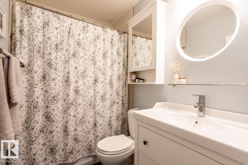 Bathroom featuring a white vanity with an integrated sink, a chrome faucet, and a round illuminated mirror - 8239 93A Avenue, Edmonton, AB - Indoor Photo Showing Bathroom