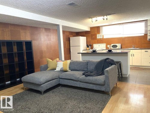 Open-concept living area featuring wood-finish flooring, a kitchen island with countertop seating, track lighting, cream cabinetry, and a full-size refrigerator - 8239 93A Avenue, Edmonton, AB - Indoor