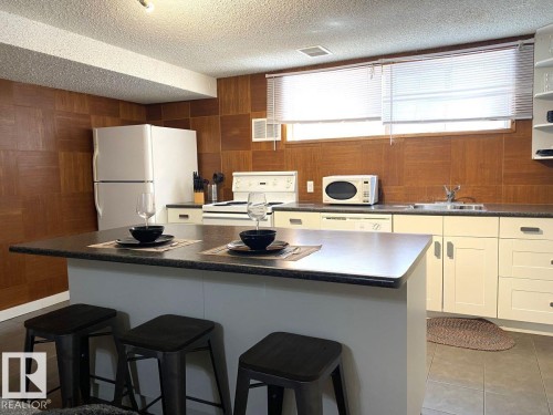 Kitchen featuring a central island with countertop seating, white cabinetry, integrated sink, and wood-finish wall panels - 8239 93A Avenue, Edmonton, AB - Indoor Photo Showing Kitchen With Double Sink