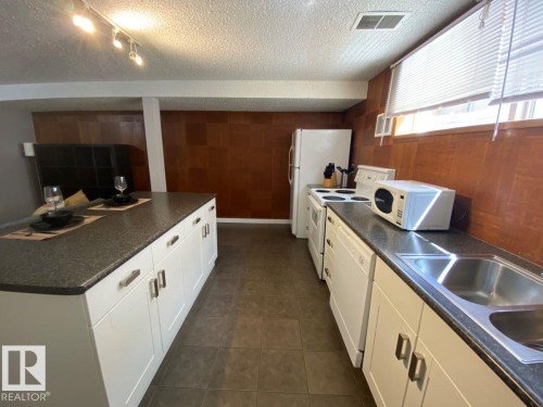 Kitchen featuring a central island with white cabinetry and dark countertops, wood-finish wall paneling, track lighting, and tiled flooring - 8239 93A Avenue, Edmonton, AB - Indoor Photo Showing Kitchen With Double Sink