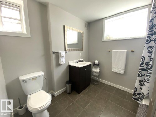 Bathroom featuring a white toilet, dark wood-finish vanity with a white basin sink, and a rectangular framed mirror - 8239 93A Avenue, Edmonton, AB - Indoor Photo Showing Bathroom