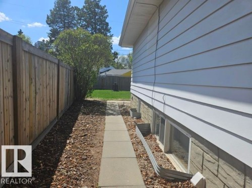 Side yard access featuring a concrete pathway, a wood privacy fence, and a planting bed with wood chip ground cover - 8239 93A Avenue, Edmonton, AB - Outdoor With Exterior