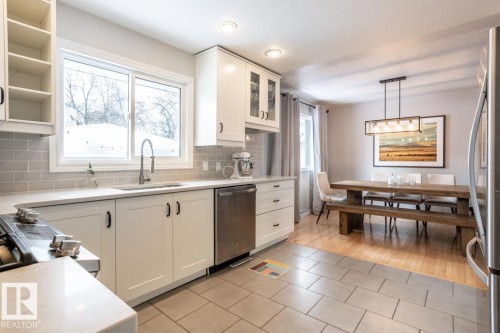 Kitchen featuring white shaker cabinetry, light-toned countertops, a stainless steel sink with a gooseneck faucet, and a grey subway tile backsplash - 8239 93A Avenue, Edmonton, AB - Indoor