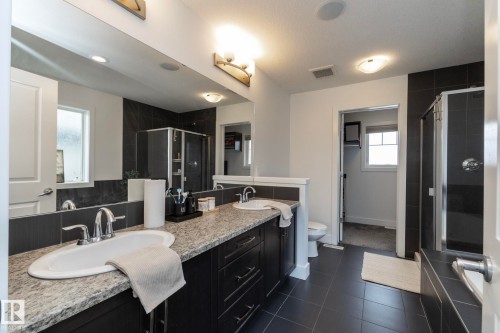 This bathroom features a double vanity with stone countertops and undermount sinks, a large mirror, and tiled floors - 14 Edgewater Terr North, St. Albert, AB - Indoor Photo Showing Bathroom