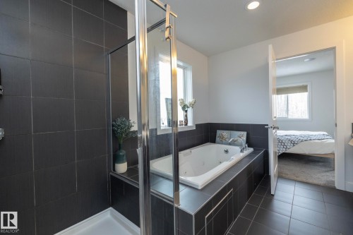 Bathroom featuring dark tiled flooring and walls, a white built-in bathtub, and a glass-enclosed shower - 14 Edgewater Terr North, St. Albert, AB - Indoor Photo Showing Bathroom