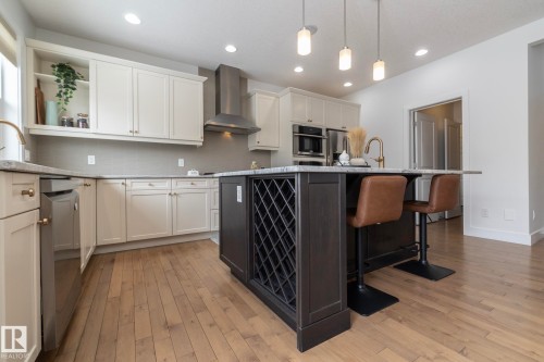 Well-appointed kitchen featuring light-toned cabinetry, light wood floors, stainless steel appliances, a center island with a built-in wine rack, and pendant lighting - 14 Edgewater Terr North, St. Albert, AB - Indoor Photo Showing Kitchen With Upgraded Kitchen