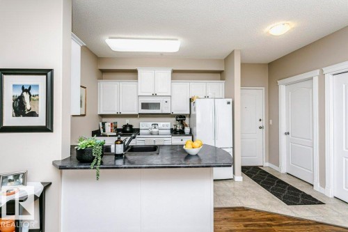 Kitchen featuring white cabinetry, dark countertops, a built-in microwave, and a double-basin sink - 323 16807 100 Avenue, Edmonton, AB - Indoor Photo Showing Kitchen With Double Sink