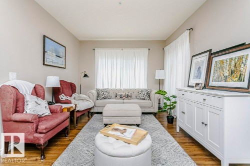 Spacious living area featuring wood-finish flooring, neutral wall tones, and ample natural light from multiple windows - 323 16807 100 Avenue, Edmonton, AB - Indoor Photo Showing Living Room
