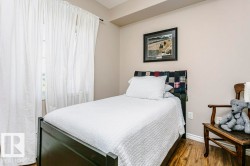 Bedroom featuring wood-finish flooring, neutral wall tones, and a window with white drapes - 