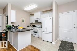 Kitchen featuring white cabinetry, black countertops, and white appliances - 