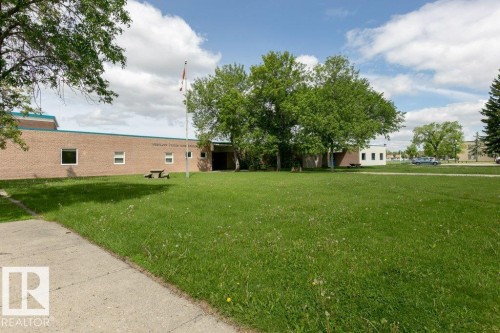Brick exterior building with multiple windows, featuring a flag pole and mature trees - 323 16807 100 Avenue, Edmonton, AB - Outdoor