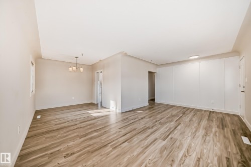 Open-concept living space featuring wood-finish flooring, a contemporary chandelier, a window with natural light, and a paneled accent wall with integrated lighting - 13124 83 Street, Edmonton, AB - Indoor Photo Showing Other Room