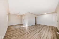 Open-concept living space featuring wood-finish flooring, a contemporary chandelier, a window with natural light, and a paneled accent wall with integrated lighting - 