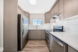 Modern kitchen featuring light wood-finish cabinetry, stainless steel appliances, white subway tile backsplash, light-colored countertops, and wood-finish flooring - 