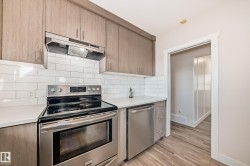 Modern kitchen featuring wood-finish cabinetry, white subway tile backsplash, white countertops, and stainless steel appliances including a range and dishwasher - 