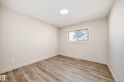 Room with wood-finish flooring, light-toned walls, white baseboards, and a single window with white trim - 