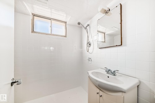Bathroom featuring a white tiled shower area, a single vanity with storage, a rectangular mirror, a window providing natural light, and a chrome shower fixture with a handheld sprayer - 13124 83 Street, Edmonton, AB - Indoor Photo Showing Bathroom
