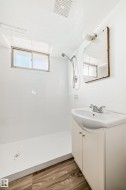 Bathroom featuring a walk-in shower with white tile surround, a built-in window, and a white vanity with an integrated sink - 