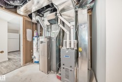 Utility area featuring a water heater and furnace with exposed ductwork, concrete flooring, and an open doorway revealing wood-finish flooring - 