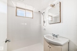 Bathroom featuring a white tiled shower area, a single vanity with storage, a rectangular mirror, a window providing natural light, and a chrome shower fixture with a handheld sprayer - 