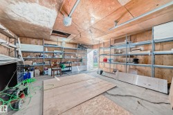 Spacious utility area featuring exposed plywood walls, a concrete floor, and extensive metal shelving for storage - 
