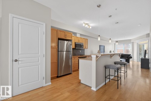 Kitchen featuring wood-finish cabinetry, stainless steel appliances, breakfast bar, pendant lighting, and wood-finish flooring - 614 10503 98 Avenue, Edmonton, AB - Indoor Photo Showing Kitchen