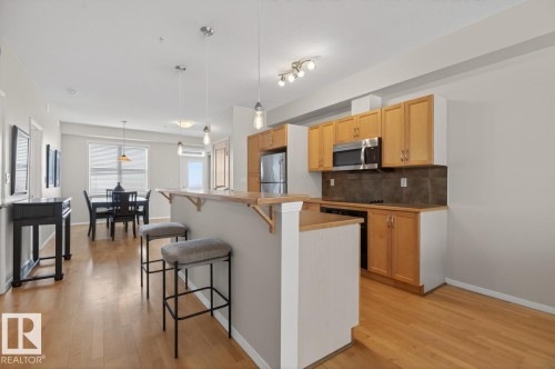 Open-concept kitchen featuring wood-finish cabinetry, stainless steel appliances, and a breakfast bar - 614 10503 98 Avenue, Edmonton, AB - Indoor Photo Showing Kitchen With Upgraded Kitchen